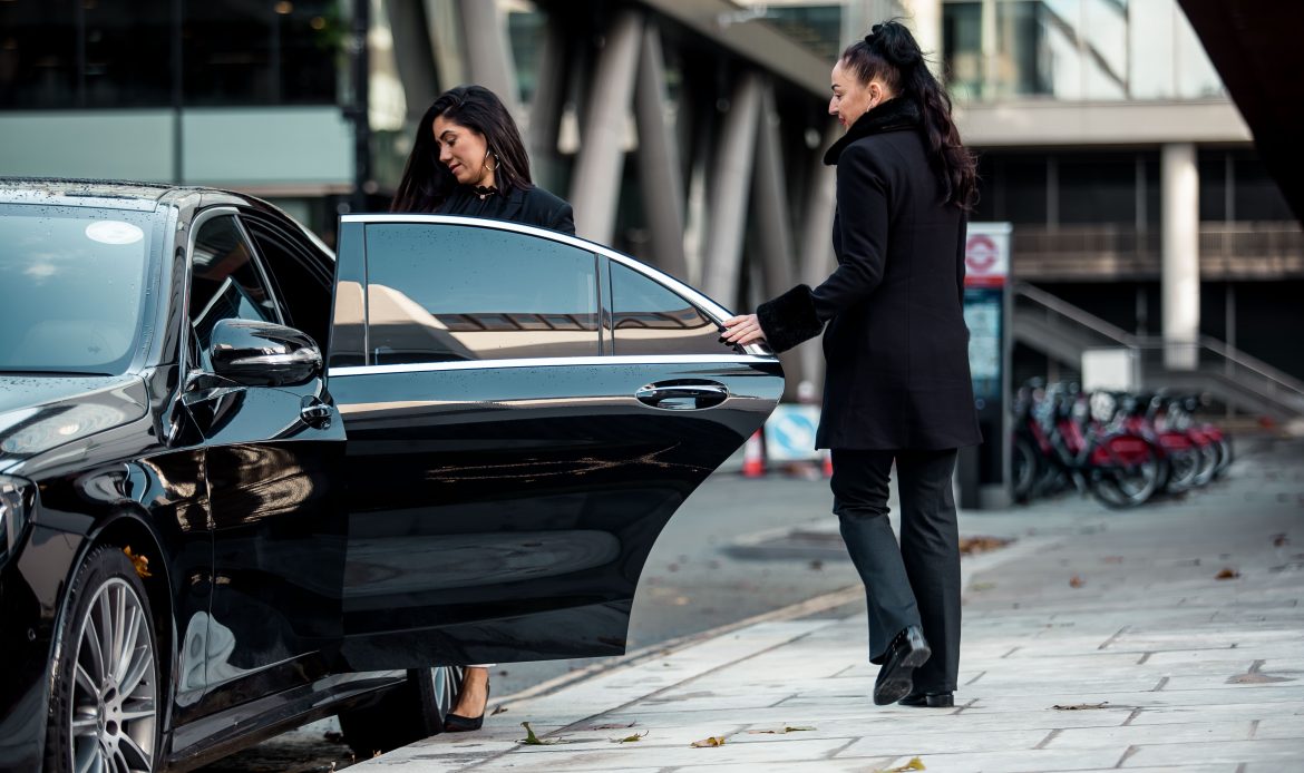 Chauffeur holding the rear door of a black sedan open for a passenger