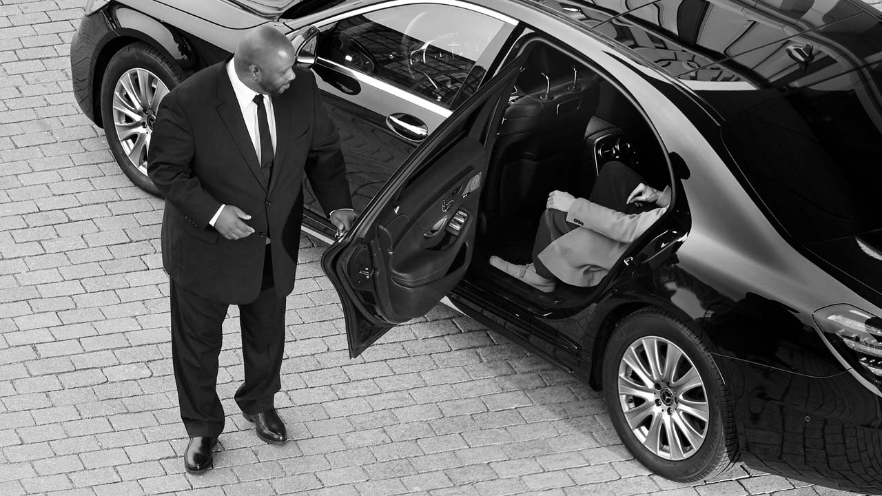 Chauffeur beside an open sedan door as a passenger settles into the rear seat